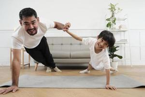 ung asiatisk thai far härlig tåg henne liten son till övning och praxis yoga på levande rum golv tillsammans för friska kondition och friskvård, Lycklig inhemsk Hem livsstil på familj helger. foto