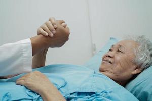 läkare håller händerna asiatisk äldre kvinna patient, hjälp och vård på sjukhus. foto