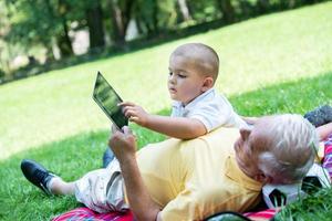 farfar och barn i parkera använder sig av läsplatta foto