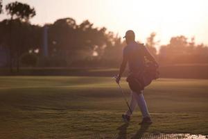 golfspelare gående och bärande golf väska på skön solnedgång foto