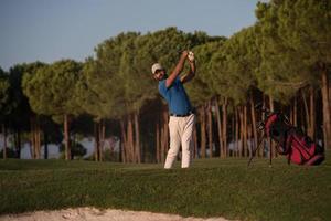 golfspelare slå en sand bunkra skott på solnedgång foto