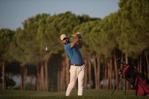 golfspelare slå en sand bunkra skott på solnedgång foto