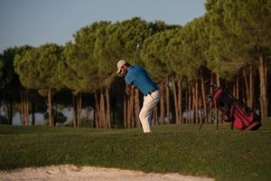 golfspelare slå en sand bunkra skott på solnedgång foto