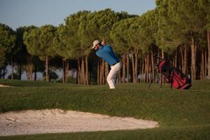 golfspelare slå en sand bunkra skott på solnedgång foto