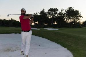 golfspelare slå en sand bunkra skott på solnedgång foto