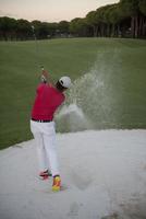 golfspelare slå en sand bunkra skott på solnedgång foto