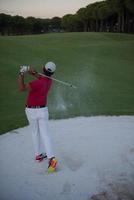 golfspelare slå en sand bunkra skott på solnedgång foto