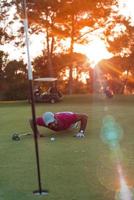 golf spelare blåser boll i hål med solnedgång i bakgrund foto