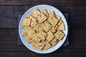 utsökt friska småkakor crackers med lin frön och sesam frön på en tallrik. bakgrund av en friska mellanmål mat, mörk rustik trä- tabell. kopia Plats. foto