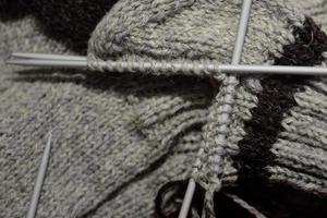 närbild av en halvfärdig stickat grå ull- grov strumpa med stickning nålar, som är stickat förbi hand. foto