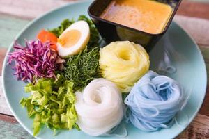 thai mat utsökt och skön mat ris nudel färgrik eller thai ris vermiceller nudel och fisk krabba curry soppa sås med vegetabiliska på tallrik trä tabell foto