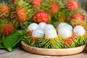 färsk och mogen rambutan ljuv tropisk frukt skalad rambutan med blad på trä- tallrik, rambutan frukt skörda från de trädgård rambutan träd foto