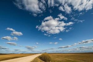 blå himmel bakgrund med stor vit randig moln i fält med grus väg. . blå himmel panorama Maj använda sig av för himmel ersättning foto