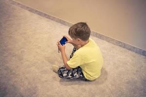 små pojke använder sig av smart telefon medan Sammanträde på de golv. foto