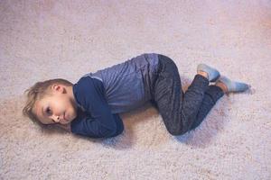små pojke avkopplande medan liggande ner på matta på Hem foto