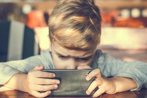 små pojke tittar på tecknade serier på smart telefon. foto