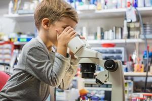 liten pojke ser genom mikroskop i laboratorium. foto