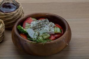 grekisk sallad i en skål på trä- bakgrund foto