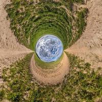 blå himmel boll i mitten av virvlande väg med gräs. inversion av mycket liten planet omvandling av sfärisk panorama 360 grader. krökning av Plats. foto