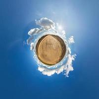 liten planet i blå himmel med sol och vackra moln. transformation av sfäriskt panorama 360 grader. sfärisk abstrakt flygfoto. utrymmets krökning. foto