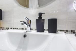 keramisk vatten kran handfat med kran med svart tvål och schampo dispensrar i dyr badrum foto