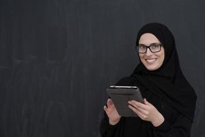ung arab affärskvinna i traditionell kläder eller abaya innehav läsplatta dator foto