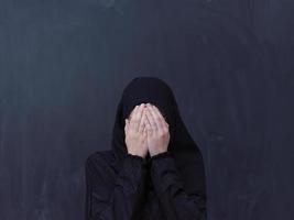 muslim kvinna framställning traditionell bön till Gud i främre av svart svarta tavlan foto