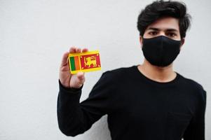 asiatisk man ha på sig Allt svart med ansikte mask håll sri lanka flagga i hand isolerat på vit bakgrund. coronavirus Land begrepp. foto