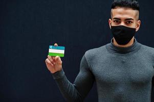 mitten östra man i grå turtleneck och svart ansikte skydda mask visa uzbekistan flagga isolerat bakgrund. foto