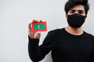 asiatisk man ha på sig Allt svart med ansikte mask håll maldiverna flagga i hand isolerat på vit bakgrund. coronavirus Land begrepp. foto