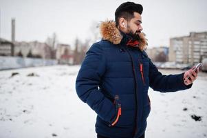 skägg indisk man ha på sig jacka i kall vinter- dag. han tala mobil telefon förbi trådlös hörlurar. foto