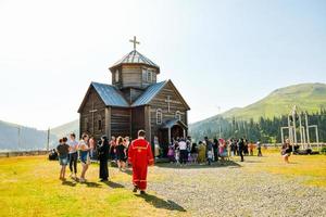 bakhmaro, georgien, 2022-präst i röd täcka promenad förbi bakhmaro kyrka till söndag massa med by människor utanför socialisera foto