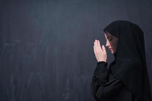 muslim kvinna framställning traditionell bön till Gud i främre av svart svarta tavlan foto