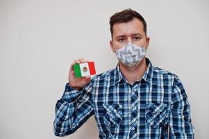 man i rutig skjorta visa mexico flagga kort i hand, ha på sig skydda mask isolerat på vit bakgrund. amerikan länder coronavirus begrepp. foto