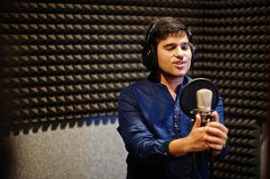 ung asiatisk sångare man med mikrofon inspelning låt i spela in musik studio. foto