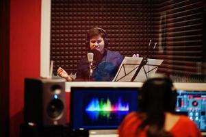 ung asiatisk sångare man med mikrofon inspelning låt i spela in musik studio med ljud producent. foto