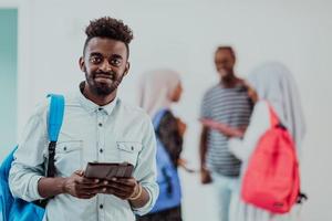 universitet livsstil stilig ung studerande man innehav en läsplatta dator och leende medan stående mot universitet med hans vänner ha en team möte i de bakgrund. hög kvalitet Foto