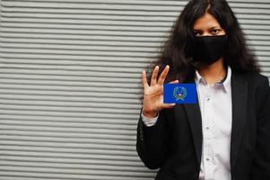 asiatisk kvinna på formell ha på sig och svart skydda ansikte mask håll pohnpei flagga på hand mot grå bakgrund. coronavirus på Land begrepp. foto