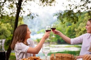 Lycklig kvinnor toasting röd vin glas under franska middag fest utomhus- foto