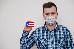 man i rutig skjorta visa puerto rico flagga kort i hand, ha på sig skydda mask isolerat på vit bakgrund. amerikan länder coronavirus begrepp. foto