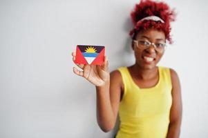 afrikansk amerikan kvinna med afro hår, ha på sig gul undertröja och glasögon, håll antigua och barbuda flagga isolerat på vit bakgrund. foto