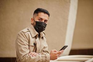 eleganta kuwaiti man på dike täcka ha på sig svart ansikte mask under covid pandemia med telefon. foto