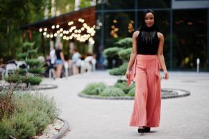 modern afrikansk amerikan kvinna i persika byxor och svart blus utgör utomhus. foto