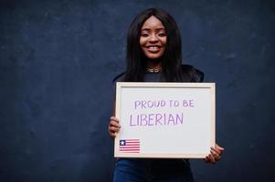 stolt till vara liberian. modern afrikansk kvinna håll styrelse med Liberia flagga. foto