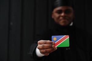 afrikansk man ha på sig svart durag håll namibia flagga på hand isolerat mörk bakgrund. foto