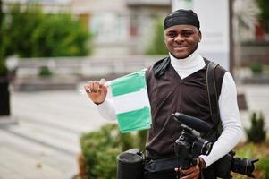 ung professionell afrikansk amerikan videographer innehav professionell kamera med nigerian flaggor i händer. foto