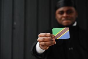 afrikansk man ha på sig svart durag håll tanzania flagga på hand isolerat mörk bakgrund. foto