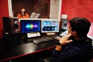 ung asiatisk sångare med mikrofon inspelning låt i spela in musik studio med ljud producent. foto
