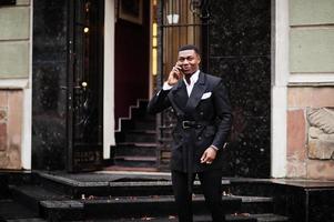 porträtt av ung och stilig afrikansk amerikan affärsman i kostym tala på mobil telefon, förbereda för möte. foto