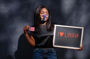 jag kärlek liberia. modern afrikansk kvinna, ha på sig hand tillverkad ansikte mask håll svarta tavlan med liberian flagga. foto